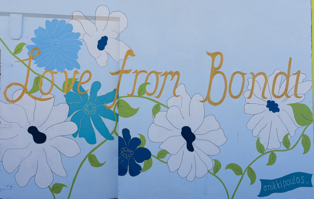 A colorful mural featuring the phrase 'Love from Bondi' in decorative lettering, surrounded by floral illustrations in blue, white, and green.